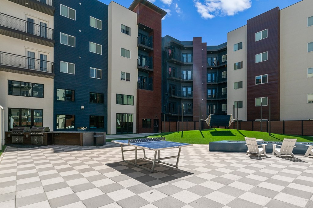 A large checkerboard patterned patio with a table and chairs in front of apartment buildings.