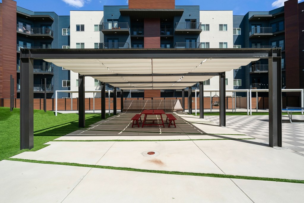 A patio with a white canopy and red chairs is in front of a building.