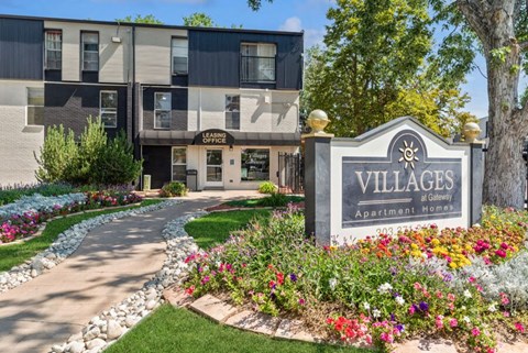 a building with a sign that says villages apartments with flowers in front of it
