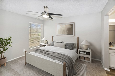 Two-Bedroom Apartments in Arlington, TX - Woodcreek - Bright Bedroom With Ceiling Fan, Nightstands With Lamps, Large Window With Blinds, And Neutral Carpet.