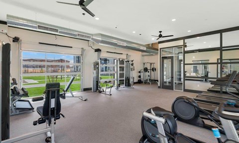 Westgate, AZ, Pet-Friendly Apartments - Glen 91 - A Modern Fitness Center Features Cardio Machines, Weight Equipment, Large Windows, Exposed Ductwork, And Ceiling Fans.