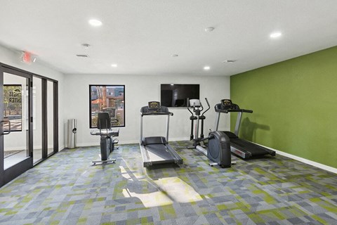 Studio Apartments Eastside Tucson, AZ - Tanque Verde - A Fitness Center With Treadmills, Exercise Bike, Elliptical Machine, Wall-Mounted Television, And Floor-to-Ceiling Windows.