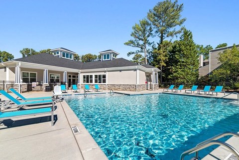 Raleigh, NC, Pet-Friendly Apartments - Bridges at North Hills - A Swimming Pool With A Spacious Sun Deck, Lounge Chairs, Trees, And A Clubhouse Building.