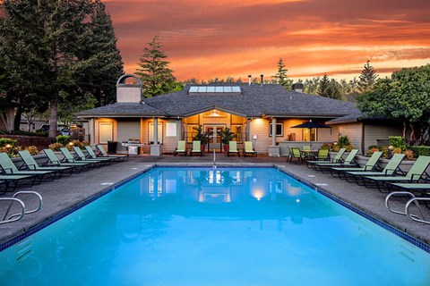 Hillsboro, OR pet Friendly Apartments - Club at Tanasbourne - Resort Style Outdoor Pool With Lounge Chairs, Clubhouse Patio, And Sunset Sky Over Landscaped Community Grounds