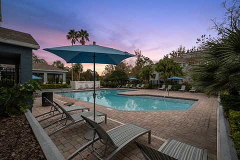 Westside Jacksonville, FL, Apartments Near Oakleaf Town Center - Westland Park - A Swimming Pool Area Features Lounge Chairs, Blue Umbrellas, And Palm Trees.