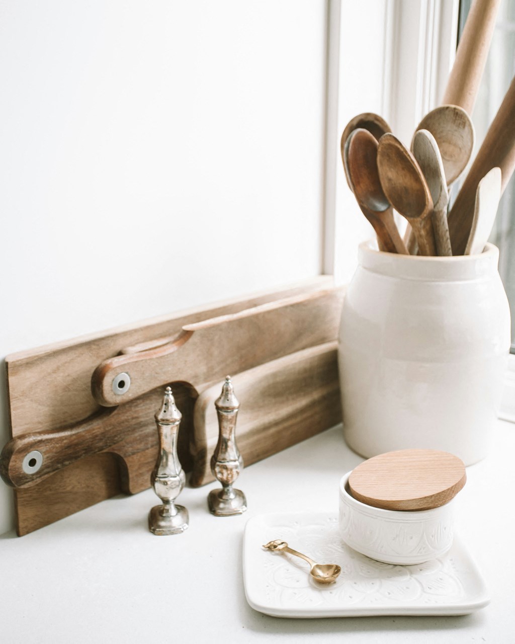 a set of wooden spoons on a window sill next to a wooden cutting board