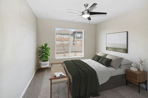 Three-Bedroom Apartments in Garland, TX - The Belmont at Duck Creek - A Bedroom With A Ceiling Fan, Window With Blinds, Nightstand Decor, Wall Art, And Potted Plant.