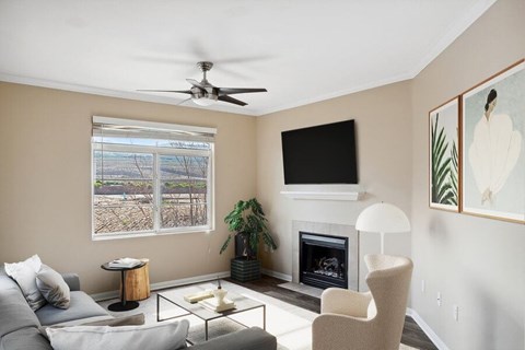 A living room with a grey couch, a fireplace, a ceiling fan, and a painting on the wall.