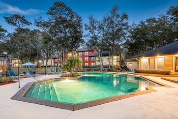 A swimming pool surrounded by trees and buildings at dusk.