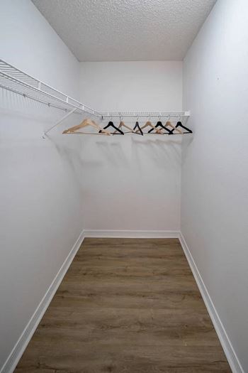 A white closet with a wooden floor and clothes hanging on a rail.