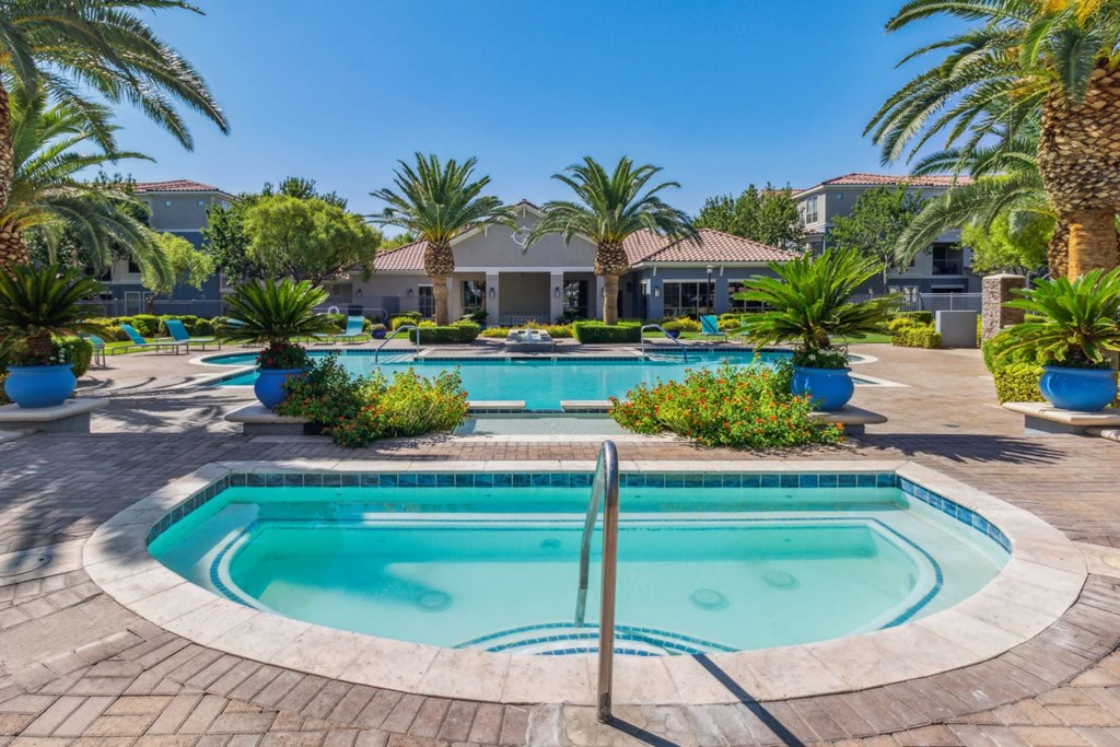A large outdoor swimming pool surrounded by palm trees and a residential area.