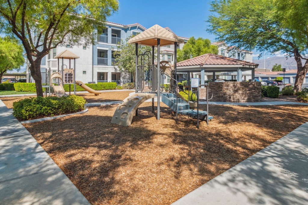 A playground with a swing set and a slide in the foreground and apartment buildings in the background.