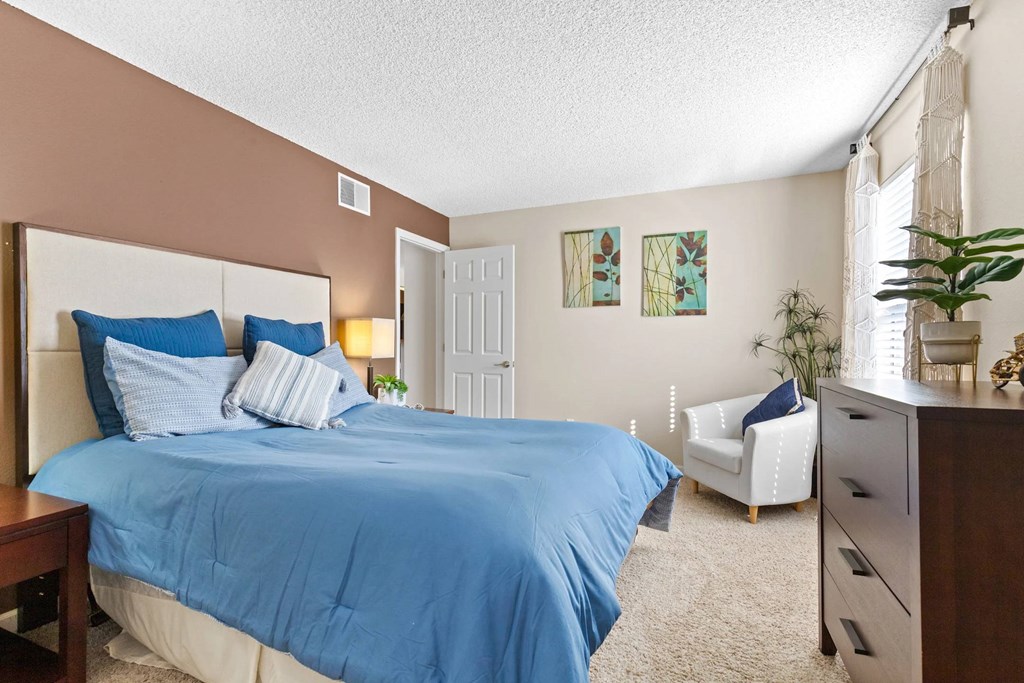 A bedroom with a blue bedspread and a white chair.