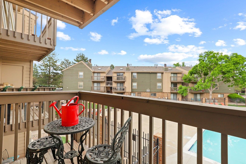 A red watering can sits on a table on a balcony.