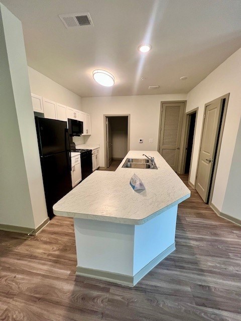 A kitchen with a black fridge and microwave, a white island, and a sink.at Arbours at Moores Mill, Huntsville