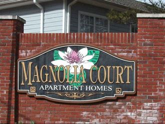 a magnolia court apartment homes sign on a brick wall
