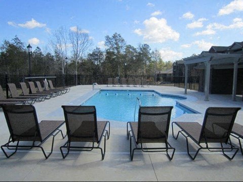 A pool surrounded by chairs and trees.