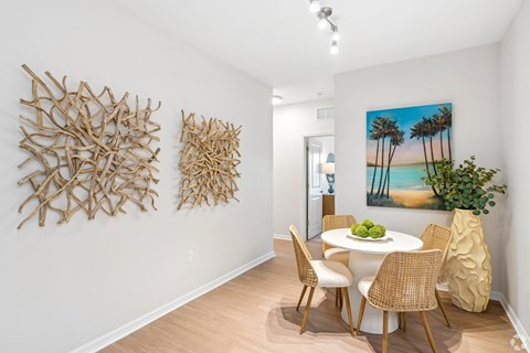 A dining room with a white table and chairs, a painting of a beach scene, and two pieces of artwork on the wall.