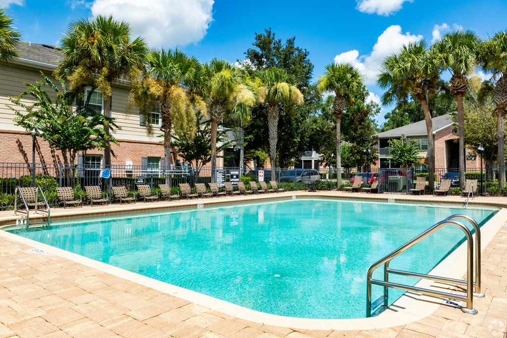 A swimming pool surrounded by palm trees and a building in the background.