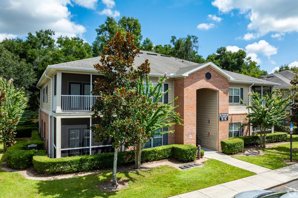 A house with a brown brick facade and a grey roof is surrounded by greenery.