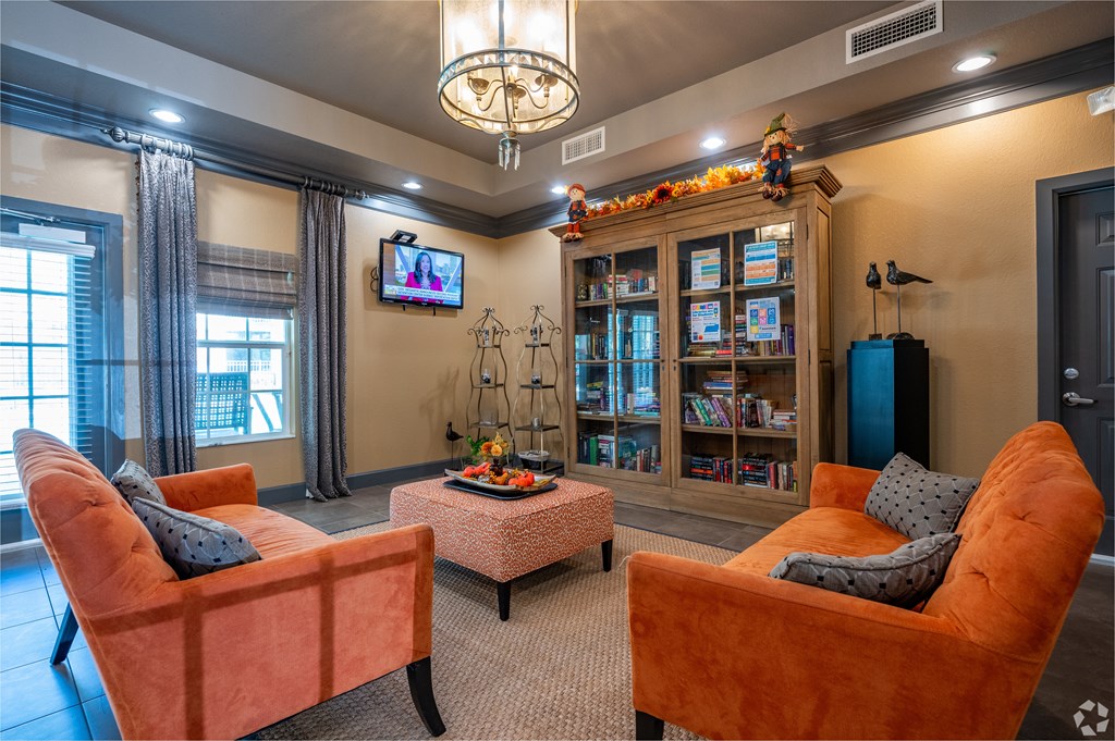 Two orange chairs are in front of a bookcase in a room.