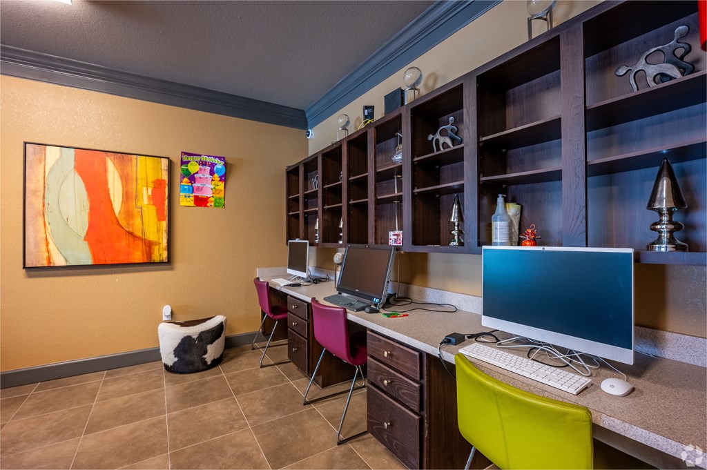 A room with a desk, computer, and a painting on the wall.