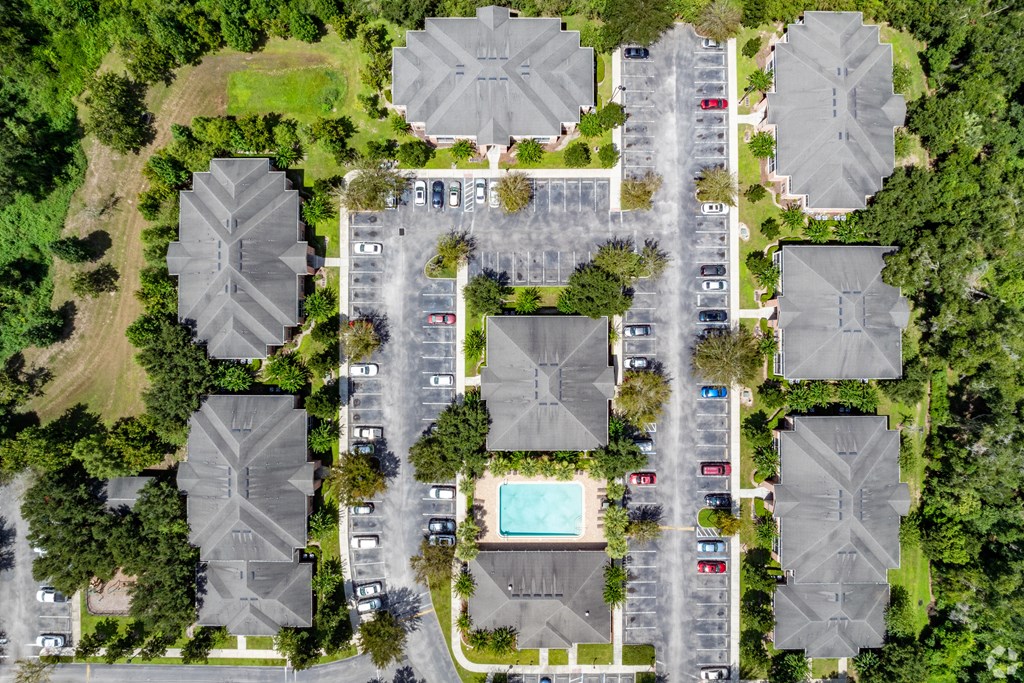 A bird's eye view of a residential area with houses, cars, and a pool.