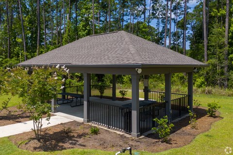 A gazebo with a black roof and a white railing is surrounded by trees.