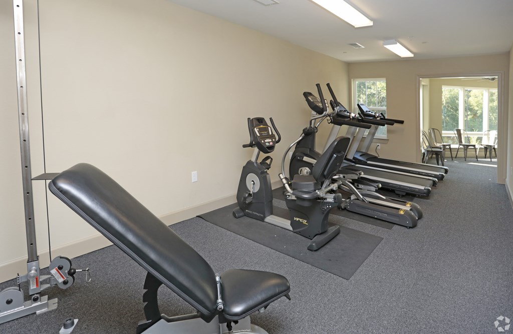 A gym with a row of treadmills and a row of stationary bikes at Arbours at Tumblin Creek ~ Active 55+ Adult Community, Gainesville, Florida