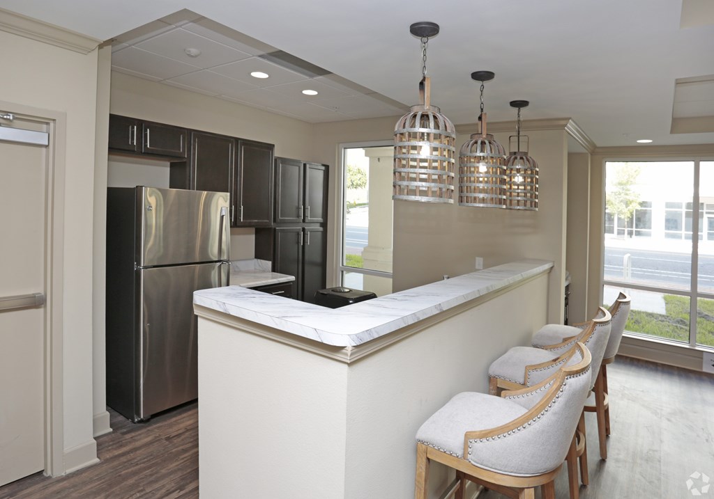 A kitchen with a refrigerator, bar stools, and pendant lights at Arbours at Tumblin Creek ~ Active 55+ Adult Community, 32608