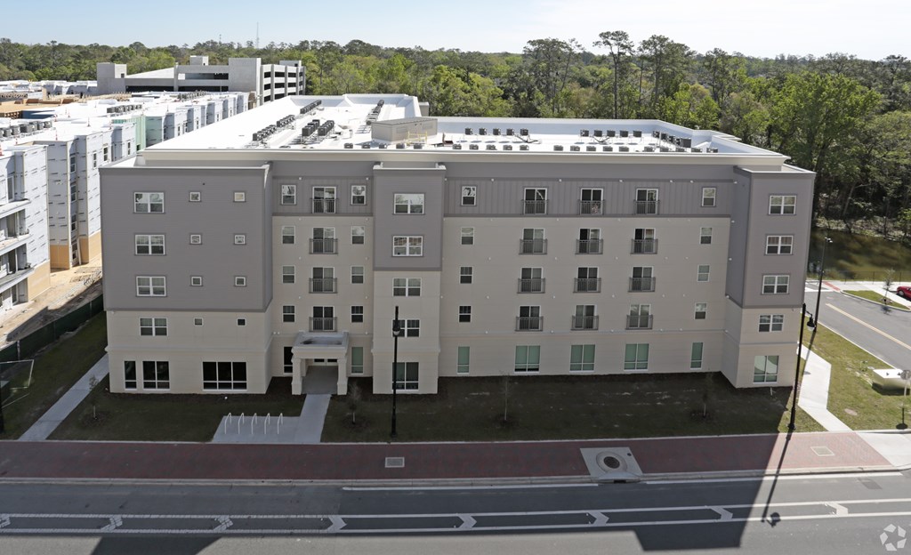 A large, modern building with a flat roof and multiple windows is surrounded by a parking lot and other buildings at Arbours at Tumblin Creek ~ Active 55+ Adult Community, Gainesville, FL