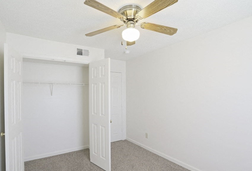 an empty bedroom with a ceiling fan and a closet