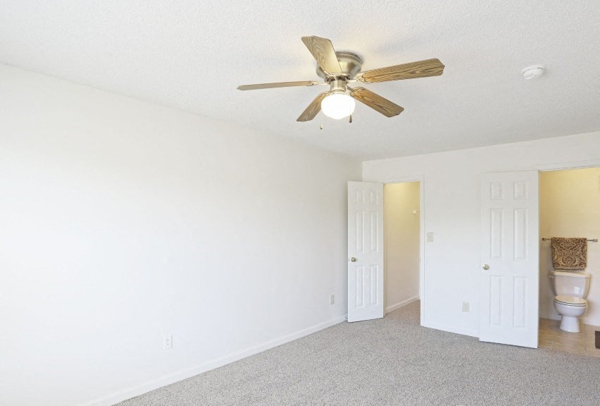 an empty living room with a ceiling fan and a toilet
