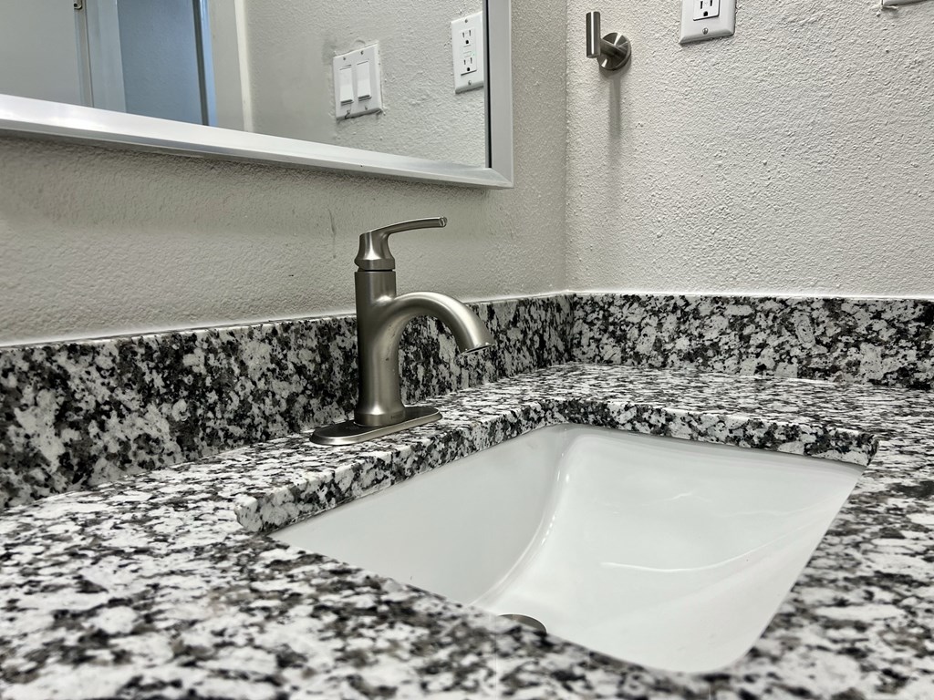 a sink in a bathroom with granite counter top and a mirror