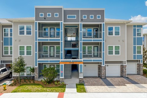 A modern apartment building with a grey and blue exterior and a red and white striped awning.