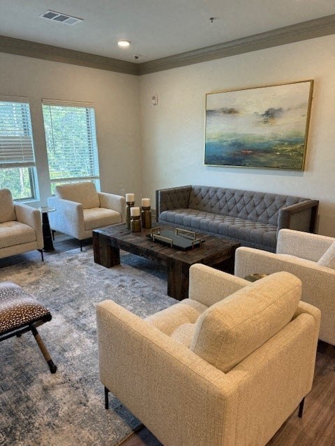 A living room with a grey sofa, a grey coffee table, a grey armchair, a white chair, and a painting on the wall.