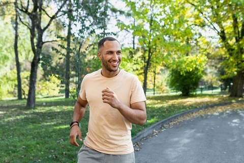A man in a beige shirt and grey shorts is running on a path in a park.
