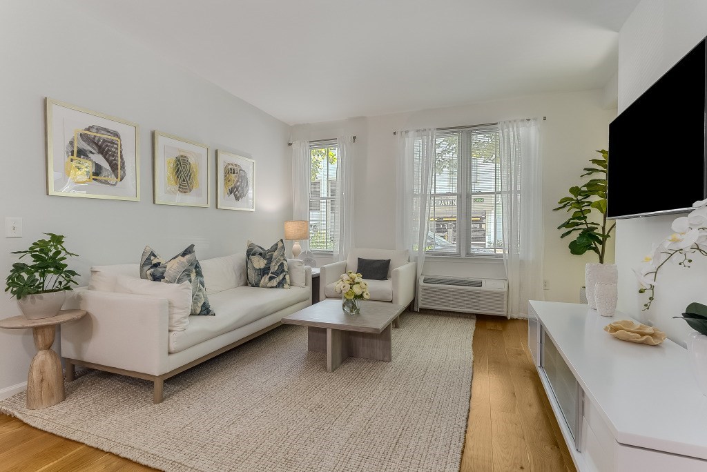 A living room with a white couch, a coffee table, and a flat screen TV mounted on the wall.