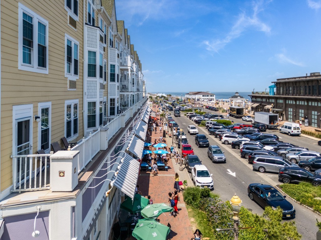 A street view of a sunny day with cars parked on the side of the road and people walking on the sidewalk.