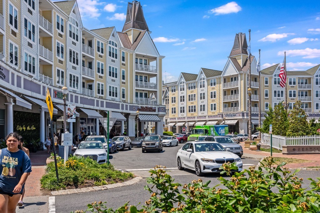 A woman in a blue shirt is walking on a street with a white car parked on the side.