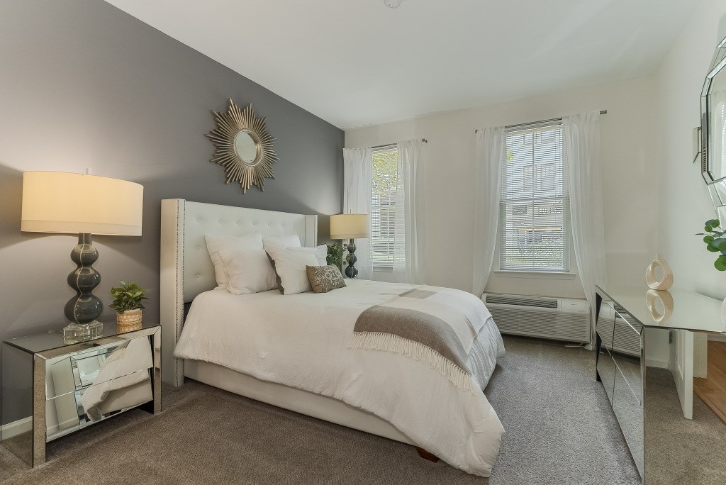 A bedroom with a large bed, a nightstand with a lamp, and a mirror on the wall.