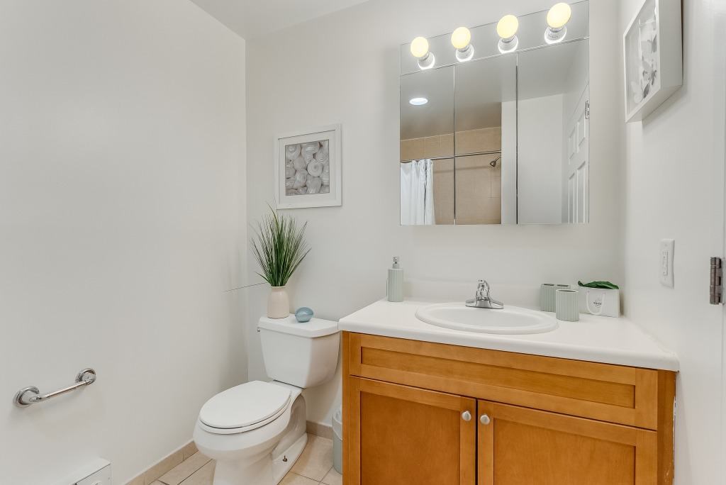 A bathroom with a white toilet, a wooden cabinet, and a mirror with lights above it.
