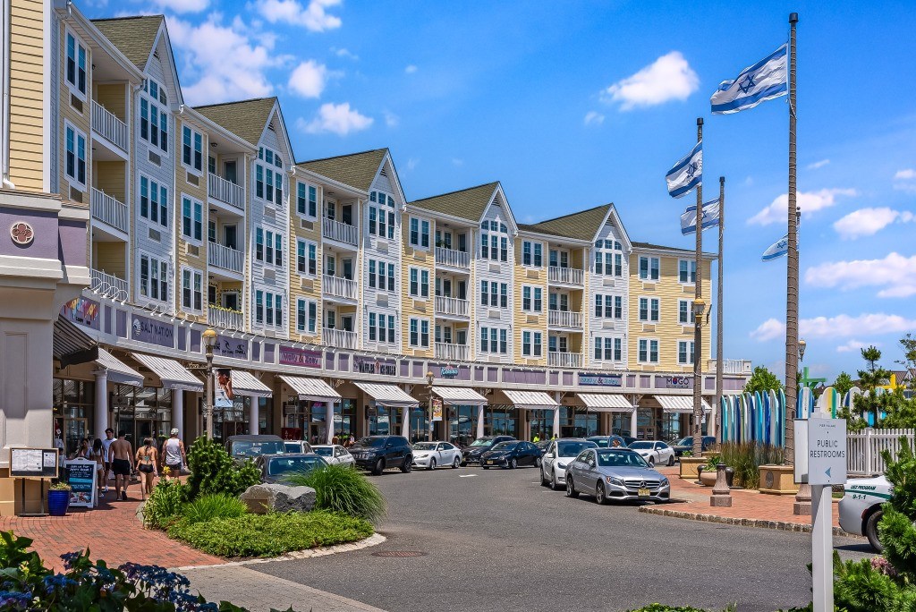 A sunny day at a bustling shopping center with cars parked and people walking.