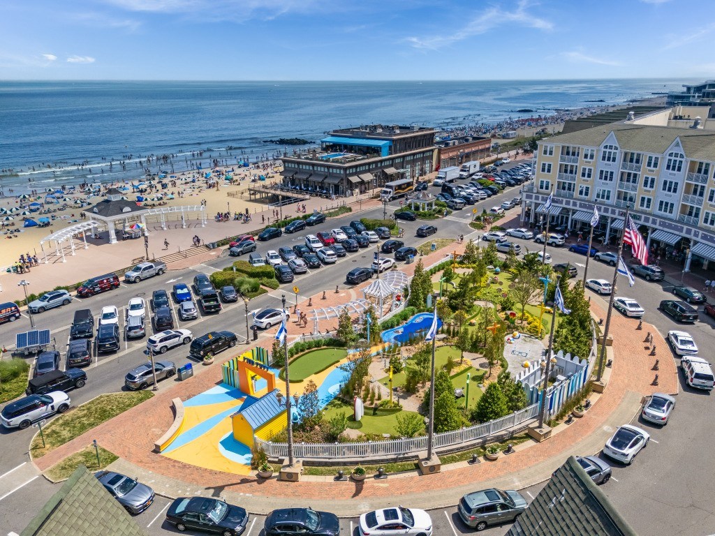 A view of a beachfront area with a playground, parking lot, and buildings.