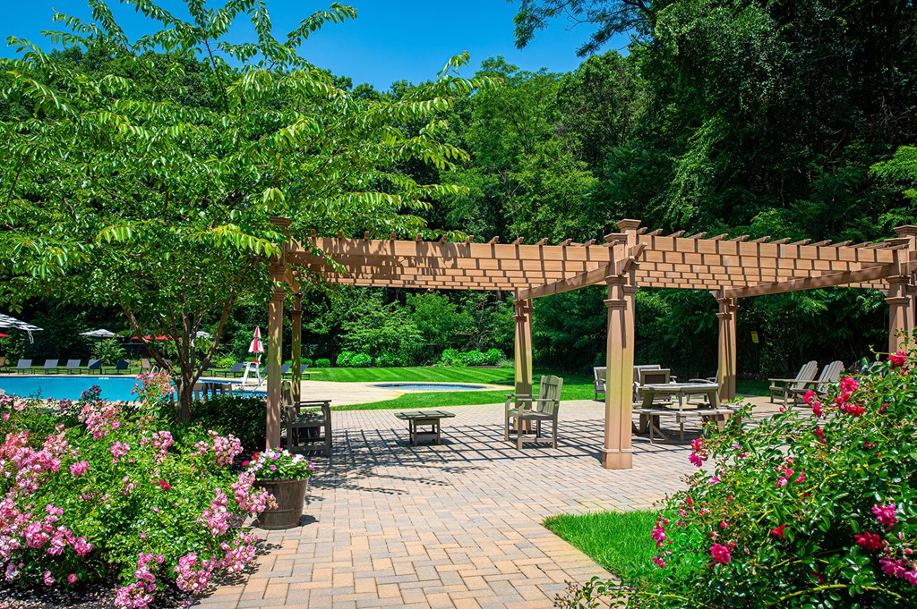 A wooden pergola is in the middle of a patio with a pool in the background at Atlantic Pointe Apartments, Atlantic Highlands, NJ 