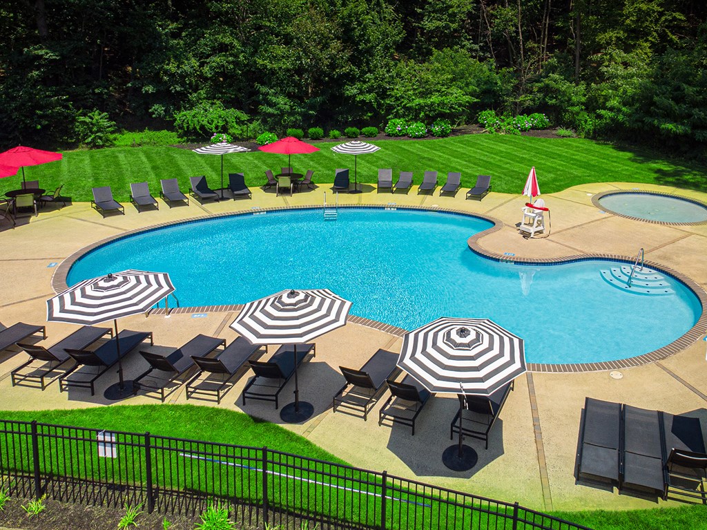 A large outdoor swimming pool surrounded by black lounge chairs and red umbrellas at Atlantic Pointe Apartments, Atlantic Highlands, NJ 07716