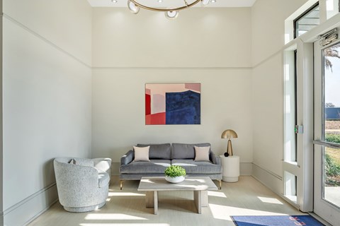 A modern living room with a grey couch, a grey armchair, a wooden coffee table, and a large abstract painting on the wall.