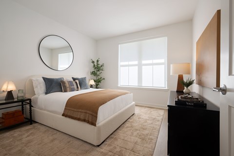 A bedroom with a large bed, a round mirror, and a black dresser.