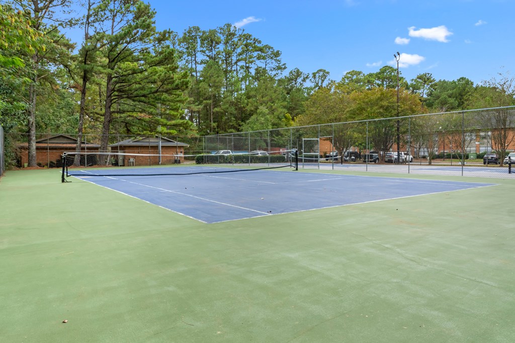 A tennis court surrounded by a fence and trees.