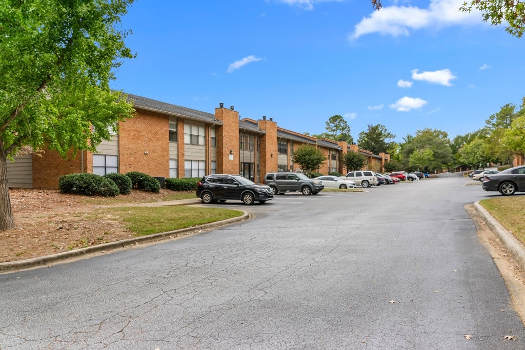A parking lot in front of a brick building with cars parked.